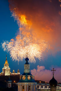 Firework display over illuminated buildings against sky at night