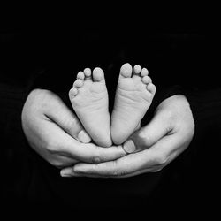 Close-up of woman hand holding baby against black background