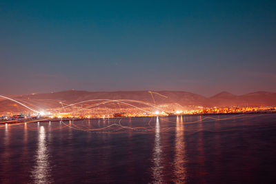 Illuminated city by sea against sky at night