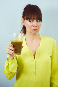 Woman having drink while standing against wall