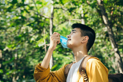 Portrait of young man drinking glass against trees