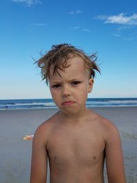 Portrait of shirtless boy standing at beach against sky