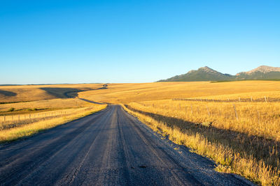Road amidst field against clear blue sky