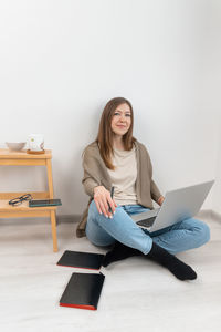 Handsome woman sitting on floor and working on a laptop. girl looking into camera. home office.