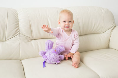 Cute baby girl sitting on sofa while playing with stuffed toy