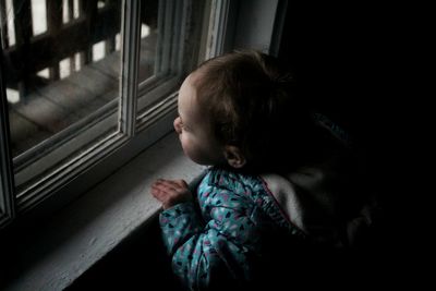 High angle view of cute girl looking through window at home