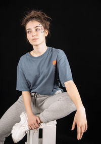 Portrait of smiling young woman sitting against black background