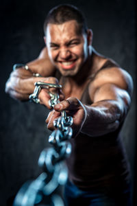 Muscular worker pulling metal chain while standing against black background