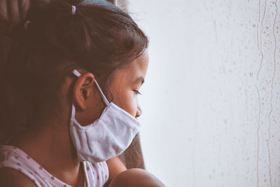 Ill girl wearing protective mask while sitting by window