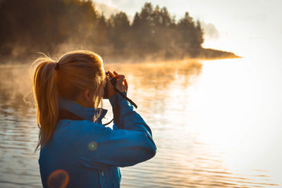 Rear view of girl photographing sea against sky during sunset