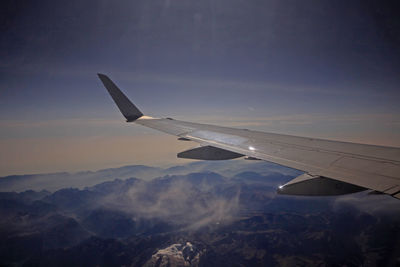 Airplane wing over landscape against sky