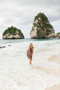 Full body image of a woman laughing at diamond beach on nusa penida.