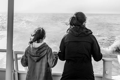 Rear view of daughter and mother looking at sea while standing by railing in ship