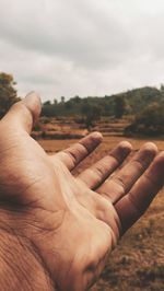 Close-up of people hand on land against sky