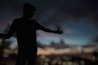 Silhouette teenage boy with arms outstretched outdoors