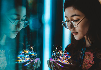 Portrait of woman looking at illuminated window