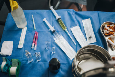 Operating table with a blue tablecloth with filled needles, used iodine gauze, anesthesia and a metal pot among other tools