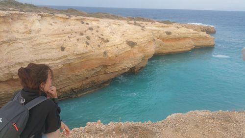 Rear view of woman standing on cliff by sea