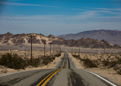 Country road leading towards mountains against sky