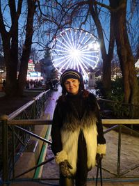 Portrait of woman standing against ferris wheel at dusk