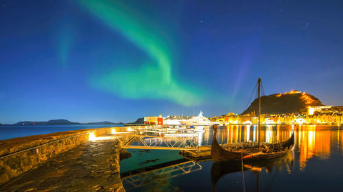 Illuminated buildings by river against sky at night