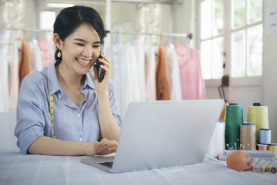 Cheerful fashion designer talking on phone at boutique