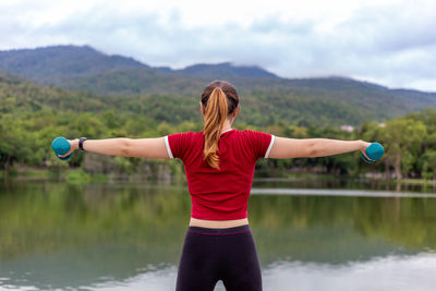 Rear view of woman with arms raised standing in lake