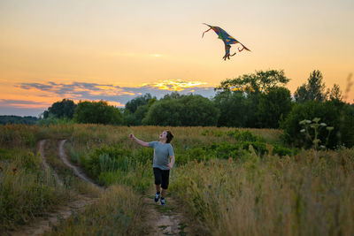 Rear view of woman walking on field against sky during sunset