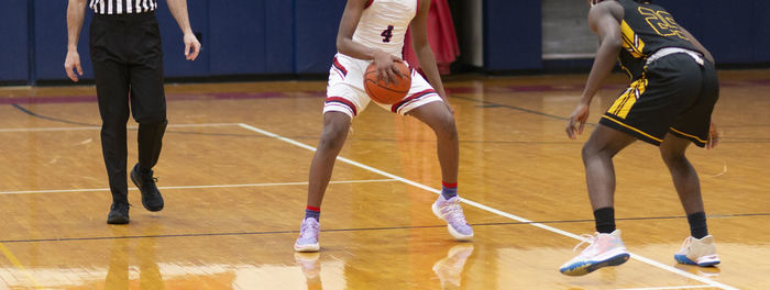 Basketball player bringing the ball up court is met by defender with the referee following the play.