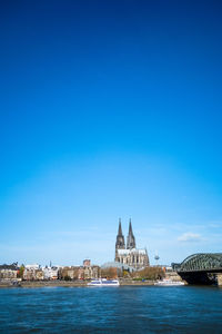 Distant view of cologne cathedral by rhine river in city against blue sky