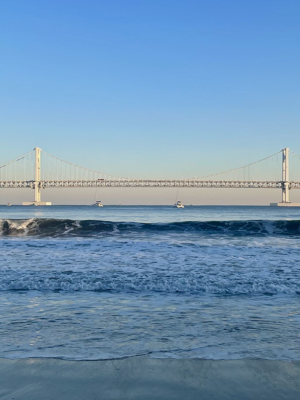 bridge, water, suspension bridge, sky, built structure, architecture, transportation, sea, travel destinations, nature, travel, clear sky, copy space, engineering, ocean, blue, tourism, horizon, cable-stayed bridge, city, scenics - nature, wave, shore, coast, beauty in nature, day, outdoors, pier, land, bay, building exterior, sunny, bay of water, tranquil scene, sunlight, beach, tranquility, motion