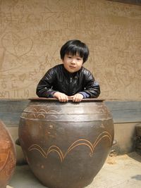 Portrait of boy sitting in container by wall