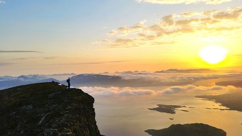 Man standing on mountains by clouds during sunset