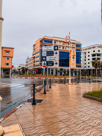 Wet street by buildings in city against sky