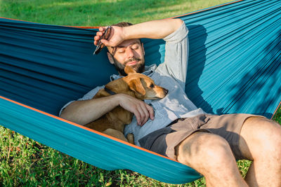 Young attractive european man is dozing in hammock with his cute little dog. sunny weekend. 