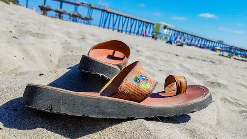 Close-up of shoes on sand at beach against sky