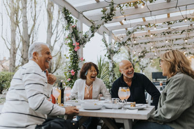 Cheerful male and female senior friends laughing while having food at restaurant