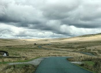 Scenic view of road amidst field against storm clouds