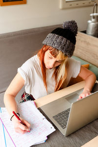 From above focused female traveler sitting at table in truck and taking notes while working on project remotely