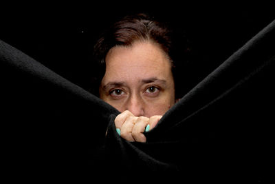 Close-up portrait of woman holding fabric against black background