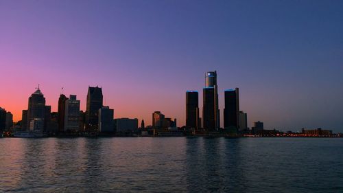 Cityscape in front of river against sky during sunset