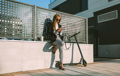 Full length of beautiful businesswoman using smart phone standing outdoors