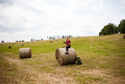 Woman sitting on hay bale against sky