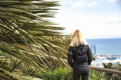 Rear view of woman standing by plants against sky