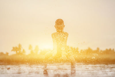 Shirtless boy splashing water in lake against sky