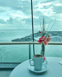 Flower vase on table by sea against sky