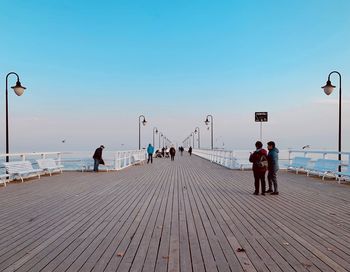 People on pier against sky during sunset