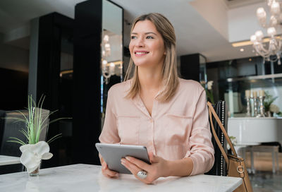 Smiling young woman using phone while standing on table