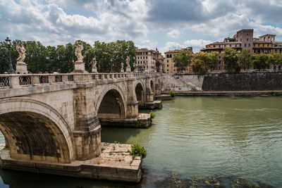 Arch bridge over river against cloudy sky