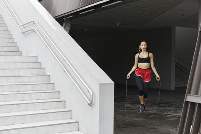 Young sportswoman jumping with rope at basement